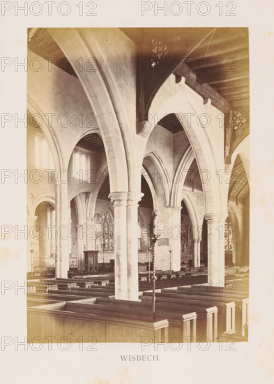 Wisbech, photograph, page, photographer: Edward Johnson, Parish Church of Saint Peter and Paul, c. 1858 - in or before 1869, Cambridgeshire, paper, albumen print, height 177 mm x width 125 mm, interior of church, parts of church interior: aisle, The image shows the interior of a church with tall stone arches and columns supporting a wooden ceiling, rows of wooden pews filling the nave, arched windows admitting light into the space, ornate stonework and carved details around the arches, a pulpit or lectern set against a wall with decorative panels and stained glass visible in the background, and a freestanding metal candleholder or stand positioned among the pews.
