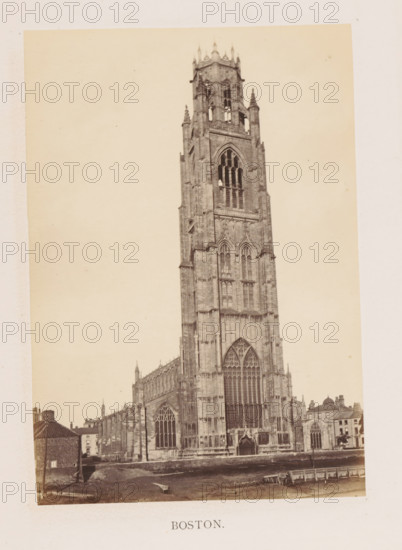 Boston, photograph, page, c. 1858 - in or before 1869, photographer, Lincolnshire, paper, albumen print, height 175 mm x width 122 mm, church (exterior), facade (of house or building), Saint Botolph's Church, A sepia-toned photograph of a tall Gothic stone cathedral tower with ornate pointed arches, large stained-glass window openings, carved stone tracery, buttresses, and pinnacles, flanked by the lower nave and aisles with rows of arched windows, adjacent smaller buildings with pitched roofs, a foreground area of bare ground and a low retaining wall, and a pale blank sky above.
