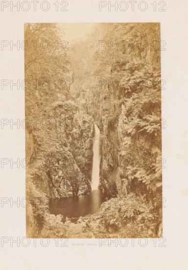 Stanley Ghyll, Eskdale, View of the Stanley Ghyll waterfall in Eskdale, photograph, page, photographer: Garnett & Sproat, Lake District, c. 1857 - in or before 1870, paper, albumen print, height 167 mm x width 106 mm, Photo opposite title page., waterfall, Cumbria, A tall, narrow sepia photograph shows a vertical rock gorge with a waterfall dropping from a slit between steep rock faces into a dark pool below, the rocky cliffs on either side covered with ferns and other vegetation, trees and leafy branches framing the upper portion, and rocky ledges and foliage surrounding the pool at the base.