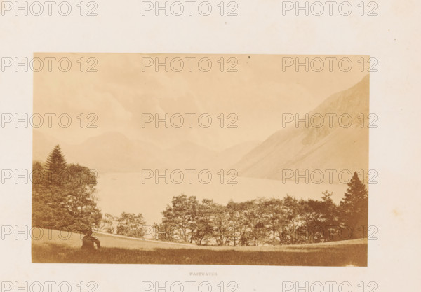 Wastwater, View of Wast Water and mountains, photograph, page, photographer: Garnett & Sproat (possibly), Lake District, c. 1857 - in or before 1871, paper, albumen print, height 105 mm x width 167 mm, lake, mountains, Wast Water, A sepia-toned landscape photograph showing a wide lake surrounded by hills and mountains, with a sloping grassy foreground where a seated figure faces the water, a line of trees along the near shore, taller trees to the left and right, and distant misty peaks fading into the sky.