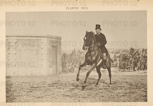 Man on a horse galloping, page, photomechanical print, number: 'Planche XXVI', maker: Jean Delton, c. 1882 - in or before 1892, paper, collotype, photoprint, height 125 mm x width 194 mm, riding a horse, ass, or mule, rider, horseman, head-gear: top hat, A sepia-toned photograph shows a man wearing a dark coat and a tall hat riding a dark horse that is captured mid-stride with one front leg raised and the other extended. The rider sits upright holding the reins, and the horse has a bridle and visible muscles along its neck and body. To the left there is a light-colored stone structure with a rectangular recessed panel and block-like corner detailing. In the background there are scattered trees and low vegetation beneath a pale sky, and the foreground shows a textured grassy or gravel ground.