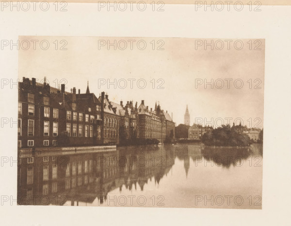 View of the Hofvijver in The Hague, page, photomechanical print, title: 'The Vyver, The Hague.', photographer: Charles L. Mitchell, The Hague, cliché maker: AW Elson & Company, Boston (Massachusetts), c. 1884 - in or before 1894, North America, Massachusetts, paper, photoaquatint, height 85 mm x width 120 mm, pond, pool, Hofvijver, A sepia-toned photograph showing a row of multi-story buildings with pitched roofs and chimneys lining a waterfront, their facades and windows reflected in the calm water below, with additional distant buildings and a tall spired tower visible along the skyline and a pale, textured sky above.