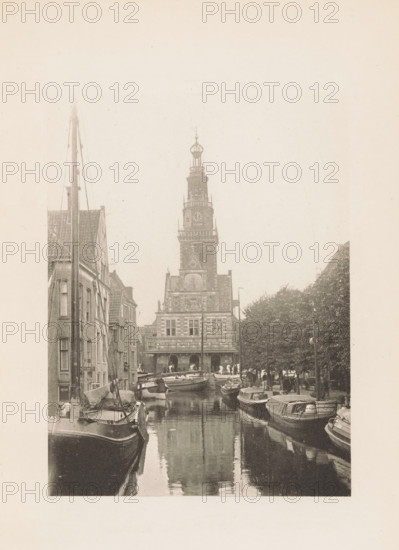 View of the Waag in Alkmaar, page, photomechanical print, title: 'The Town Weighing House, Alkmaar.', photographer: Charles L. Mitchell, Alkmaar, cliché maker: AW Elson & Company, Boston (Massachusetts), c. 1884 - in or before 1894, North America, Massachusetts, paper, photoaquatint, height 118 mm x width 90 mm, canals, waters (in village), façade (of house or building), Waag (Alkmaar), A narrow canal lined with moored boats on both sides leads toward a tall ornate building with a multi-tiered tower and decorative facade; narrow brick buildings flank the left side of the canal while trees and lamp posts line the right side, and the water reflects the boats and the tower above.