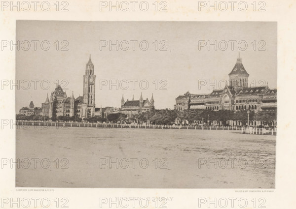 View of buildings in Mumbai, Maharashtra, India, page, photomechanical print, title: 'MODERN BOMBAY', signature, `: 'SAMPSON LOW MARSTON & CO. LTD, HÉLIOG & IMP LEMERCIER & CIE. PARIS', Mumbai, cliché maker: Lemercier & Cie., Paris, c. 1883 - in or before 1893, photographer, paper, photoaquatint, height 115 mm x width 177 mm, palace, façade (of house or building), A wide sepia-toned photograph shows a long row of ornate stone buildings with Gothic architectural features including pointed arches, steeply pitched roofs, towers, and a tall clock tower rising above the others, set behind a line of trees and a fence along a broad open foreground.