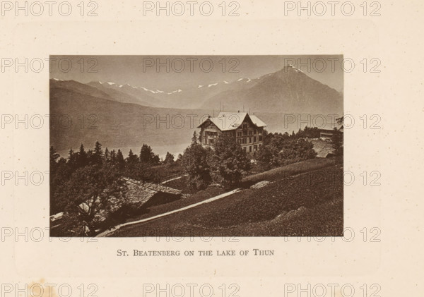 St. Beatenberg on the lake of Thun, View of a house in Beatenberg on Lake Thun, page, photomechanical print, Beatenberg, c. 1874 - in or before 1884, paper, collotype, photogravure, height 80 mm x width 128 mm, lake, mountains, Lake Thun, A sepia-toned landscape photograph bordered by a pale background shows a large multi-story chalet-style building on a hillside surrounded by trees and smaller wooden structures, with a steep grassy slope in the foreground and a winding path leading toward the building; behind it a range of mountains rises with snow patches on ridgelines and a prominent peak to the right, and a band of darker forested hills fills the midground beneath a pale sky.
