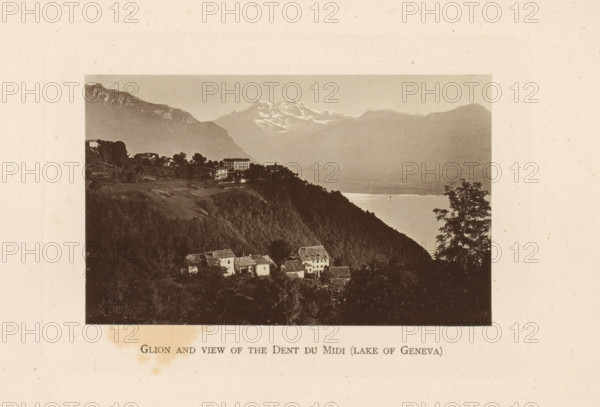 Glion and view of the Dents du Midi (lake of Geneva), View of Glion on Lake Geneva and behind it the Dents du Midi, page, photomechanical print, Montreux, c. 1874 - in or before 1884, paper, collotype, photoprint, height 83 mm x width 134 mm, lake, prospect of city, town panorama, silhouette of city, mountains, Glion, A sepia-toned photograph shows a lakeside mountain scene with a foreground of clustered houses on a forested hillside, a steep dark ridge descending toward a body of water, a tree silhouette at the right edge, distant misty mountains across the lake with a snow-capped peak visible toward the center, and a pale sky above.