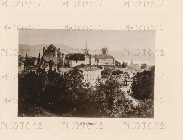 Lausanne, View of Lausanne in Switzerland, page, photomechanical print, Vaud (canton), c. 1874 - in or before 1884, paper, collotype, photoprint, height 83 mm x width 128 mm, city-view in general, 'veduta', A sepia-toned photograph shows a hillside town with clustered buildings, rooftops, and trees in the foreground and midground, a large castle-like structure with turrets and a high wall to the left, a cathedral with a tall spire and another church with a squared tower toward the center, rolling hills or mountains in the distant background, and a large dark treeline occupying the lower portion of the image.