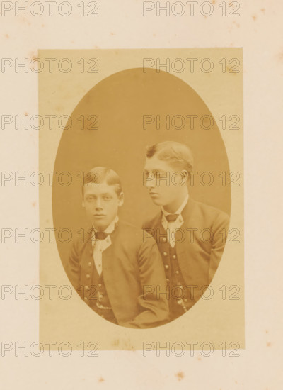 Portrait of Prince George of Wales and Prince Albert Victor of Wales, photograph, page, 1881, photographer, paper, albumen print, height 145 mm x width 99 mm, Person, George V (King of the United Kingdom), Albert Victor (Prince of the United Kingdom), prince, crown prince, A sepia-toned oval portrait mounted on a rectangular piece of paper shows two young men seated closely together, both wearing dark jackets with rows of buttons and white high-collared shirts with cravats; the man on the left faces forward with a neutral expression and neatly parted hair, while the man on the right is turned slightly toward the left with a similar neutral expression and waved hair.