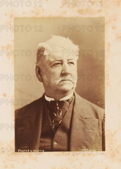 Portrait of Arthur Kennedy, photograph, page, photographer: Foster & Martin, Melbourne, c. 1880 - in or before 1881, paper, albumen print, height 153 mm x width 102 mm, Person, Arthur Kennedy, colonial governor, A sepia portrait photograph of an older man shown from the chest up, with light wavy hair styled back and a thick mustache, wearing a dark suit jacket, waistcoat, high collar, and patterned necktie; the image has a faded, aged appearance with spotting and discoloration on the surrounding mount and uneven background tones behind the subject.