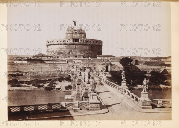View of the Bridge of Angels and the Castel Sant'Angelo in Rome, photograph, page, Rome, c. 1850 - in or before 1860, photographer, paper, albumen print, height 98 mm x width 135 mm, bridge in city across river, canal, Engelenburcht, Engelenbrug, A wide sepia-toned photograph shows a large circular stone fortress with battlements and a tiered upper structure topped by a winged statue; a bridge lined with stone balustrades and multiple classical statues and lamp posts leads toward the fortress across a body of water, with walkways, stone pedestals, and shadowed figures visible on the bridge; surrounding the fortress are low buildings, walls, and grassy embankments, and a distant landscape of low hills and scattered structures forms the background.