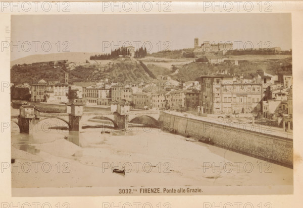 Firenze. Ponte alle Grazie, View of the Ponte alle Grazie in Florence, photograph, page, number: '3032bis.', photographer: Edizioni Brogi (possibly), Florence, c. 1878 - in or before 1888, Tuscany, paper, albumen print, height 95 mm x width 145 mm, bridge in city across river, canal, Ponte alle Grazie, A wide sepia-toned cityscape showing a river with arched stone bridges crossing it, small boats on the water, and a long stone embankment along the riverbank. Along the embankment a row of multi-story buildings with varied facades, windows, and rooftops rise from the street, with one taller building near the center-right that has decorative vertical features. Behind the riverside buildings a hillside with terraced greenery and scattered houses leads up to a ridge topped by a cluster of trees and larger structures, including a building with a tower and another with a rectangular, castle-like appearance. The sky above is pale and mostly featureless.