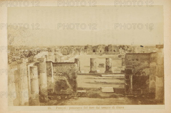 View of the Foro Civile at Pompeii, Pompeii: panorama of the foro dal tempio di Giove, photograph, page, c. 1878 - in or before 1888, photographer, paper, albumen print, height 104 mm x width 153 mm, market, landscape with ruins, Foro Civile, A sepia-toned photograph shows an ancient open area with rows of weathered stone columns and ruins. In the foreground there are tall fluted columns and rectangular stone bases, some broken and partly eroded. A wide paved walkway leads toward a central open plaza where a few short column stumps stand on square platforms. Low stone walls and fragmentary structures flank the plaza, and beyond them a distant horizontal line of additional ruined buildings and foundations is visible under a pale sky. The image has uneven staining and spotting across the surface and a faded border around the edges.