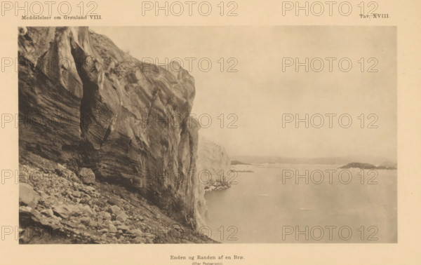 Enden og alles af en Brae, Edge of a glacier in Greenland, page, photomechanical print, number: 'Attn. XVIII.', Greenland, cliché maker: Pacht & Crone, c. 1883 - in or before 1888, photographer, paper, collotype, photoprint, height 96 mm x width 167 mm, Print after page 295., glacier (in polar regions), A sepia-toned photograph showing a large rocky cliff on the left with layered striations and rough textured surfaces, a rocky slope with scattered stones at the base, and a calm body of water extending to the right with small distant islands or rock outcrops on the horizon under a pale sky.