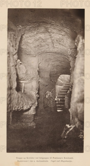 Hallway in the Catacombs of Pontian in Rome, photograph, page, inscription: 'Trappe og Korridor, Taget ved Magniumlys.', Catacombs of Pontian, c. 1876 - in or before 1886, photographer, Rome, paper, carbon print, height 168 mm x width 89 mm, catacombs, A sepia-toned vertical photograph showing a rough, arched tunnel or cavern with textured rock walls and a scalloped ceiling. The foreground includes uneven stone surfaces framing the entrance to a deeper passage. Midway into the image a set of narrow, uneven steps leads downward beside a low archway, and a small, pale vertical rod is visible against the left rock face. Light and shadow highlight the layered striations in the rock and the rough, irregular contours of the passage, with darker recesses toward the far end and softer illumination near the steps. The photograph is bordered by a light margin.