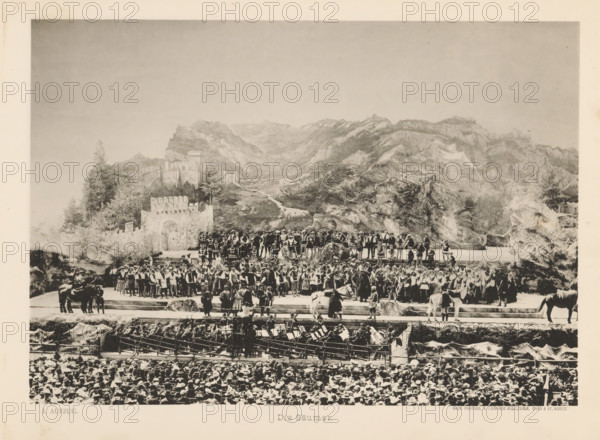 Die Säumer, View of a parade of mule drivers during the Calven-Feier in Chur, page, photomechanical print, number: 'I.', photographer: Lienhard & Salzborn, Chur, in or after 1899-05-28 - in or before 1899-06-04, paper, collotype, photoprint, height 178 mm x width 254 mm, mule, mountains, activities in the air, public festivities, eg fly-past, A wide sepia-toned scene shows a large outdoor stage set against a painted mountainous backdrop with rocky peaks and a winding valley. On the stage a dense group of people wear period costumes with varied styles including tunics, vests, capes, and hats, some holding staffs or musical instruments and a few positioned on raised platforms. Stone-like set pieces, walls, and faux vegetation frame parts of the stage, and several horses and riders stand near the edges. In front of the stage rows of seated audience members with many hats are visible, and an orchestra pit with musicians and music stands occupies the area between the stage and the audience....