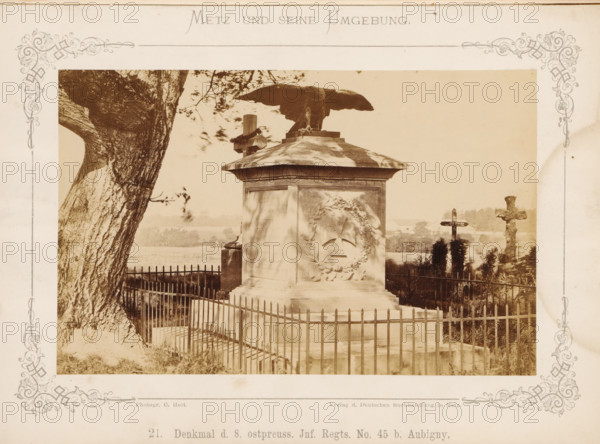 Denkmal d. 8. ostpreuss. Inf. Right. No. 45 b. Aubigny, War Memorial for the 8th East Prussian Infantry Regiment No. 45 at Aubigny near Metz, Metz und seine Umgebung, photograph, page, number: '21.', photographer: C. Holt, Lorraine, publisher: Verlag der Deutschen Buchhandlung, Metz, c. 1870 - in or before 1875, paper, albumen print, albumendruk, height 98 mm x width 154 mm, monument, statue, A sepia-toned photograph shows a fenced stone monument topped by a large sculpted eagle with outstretched wings standing on a square plinth, the plinth bearing a wreath relief on one visible face. A tall tree trunk with textured bark occupies the left foreground, and a simple metal fence surrounds the monument. In the background there are landscape elements including distant trees and fields, as well as two crosses—one plain wooden cross and one carved stone cross—visible to the right of the monument. Decorative printed borders frame the photograph on the paper mount.
