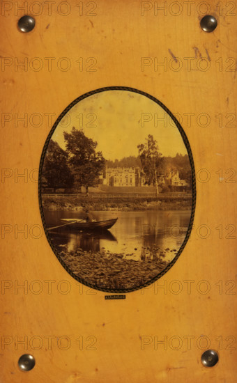 Abbotsford, View of Abbotsford House, photograph, page, c. 1858 - in or before 1868, photographer, paper, plant material, biological material, wood (plant material), albumen print, height 95 mm x width 73 mm, Photo on back cover., rowing-boat, canoe, castle, Abbotsford House, An oval sepia photograph is mounted on a worn light brown wooden board with four dark round metal studs near the corners; inside the oval, a calm river reflects a small rowboat with a seated figure holding oars, a pebbled shoreline in the foreground, a grassy riverbank with trees behind it, and a large multi-gabled building partially obscured by trees in the midground, all under a pale sky.