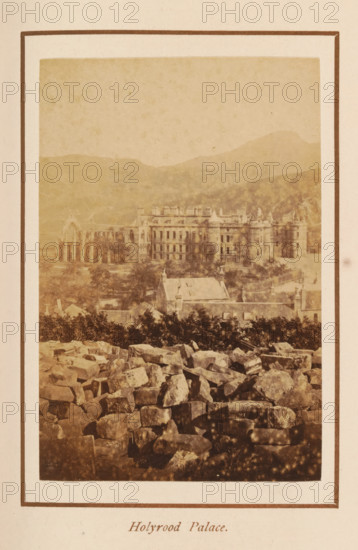 Holyrood Palace, photograph, page, photographer: George Washington Wilson, Edinburgh, c. 1885 - c. 1890, paper, albumen print, height 102 mm x width 69 mm, palace, façade (of house or building), Palace of Holyroodhouse, A sepia-toned photograph framed by a pale border shows a distant large stone building with multiple windows and towers set against rolling hills, with a ruined arched structure visible to the left of the main building; in front of the building there are smaller roofs and tree foliage, and the foreground is filled with a jumble of irregular stones and rocks.