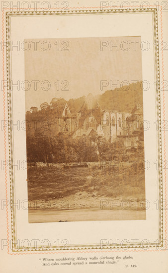 Landscape with a ruined church, photograph, page, inscription: ''Where mouldering Abbey walls o'erhang the glade, And oaks coeval spread a mournful shade.', p. 149.', c. 1885 - in or before c. 1890, photographer, paper, albumen print, albumendruk, height 108 mm x width 69 mm, Photo opposite title page., landscape with ruins, ruin of church, monastery, A sepia-toned photograph mounted on a decorative paper border shows the ruins of a large stone abbey set against a hillside, with arched windows and a circular window visible in the remaining walls; trees and dense foliage surround the ruins and extend up the slope behind them, while a grassy foreground with a small boat resting on the shore lies at the base of the scene.