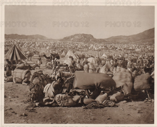 Der Berg Arafah während der jährlichen Pilgerversammlung (von Süden aus gesehen), Pilgrim camp on the plain of Arafat during the Hajj, album page, photomechanical print, This print is part of an album., number: 'XIII', photographer: Abd al-Ghaffar, Plain of Arafat, cliché maker: anonymous, 1889, Saudi Arabia, pasteboard, paper, collotype, photoprint, height 270 mm x width 360 mm, other ritual practices, Islam, Mohammedanism, tent-camp, Hajj, Period, 1888-03-30 - 1888-04-27, A wide sepia-toned scene shows a crowded encampment with rows of conical tents stretching into the distance beneath a clear sky, low hills on the horizon, numerous people dressed in draped garments walking and standing among the tents, many camels and packed animals resting on the ground with large cloths and bundles on their backs, scattered ropes and sacks in the foreground, a few makeshift awnings and poles among the tents, and groups of people gathered in clusters throughout the camp.
