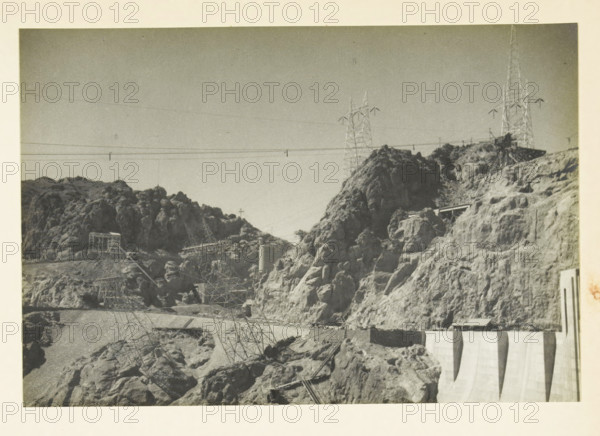 Los Angelos, California, United States: power lines, 280 kV pylons of the line to Los Angeles, photograph, title: '280 kV PIERCELS OF THE, LINE TO LOS ANGELOS', photographer: attributed to Wouter Cool, United States of America, 1936, North America, Attributed to, pasteboard, paper, gelatin silver print, height 151 mm x width 230 mm, height 315 mm x width 285 mm, pylons, A grayscale photograph showing a rocky landscape with steep, irregular cliffs and boulders, electricity transmission towers rising on the ridges and supported by lattice structures, suspended power lines strung across the scene, a concrete dam face visible at the lower right with vertical sections, small industrial structures and platforms nestled among the rocks, and a mostly clear sky above.