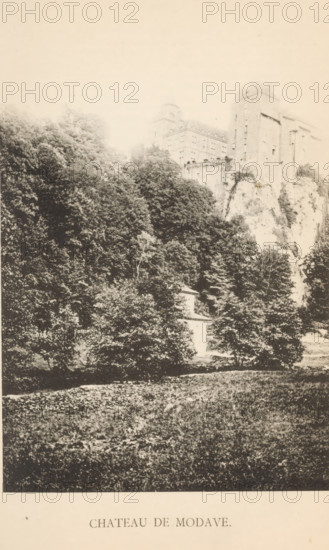 View of the castle of Modave, Chateau de Modave, page, photomechanical print, photographer: attributed to Victor Gaillard, Modave, cliché maker: attributed to Emile Aubry, Brussels, c. 1885 - in or before 1890, Attributed to, paper, collotype, photoprint, height 156 mm x width 104 mm, castle, A tall stone building with multiple levels and a tower stands partially obscured by dense trees and rocky cliffs, with foliage covering much of the hillside below and a grassy area in the foreground.