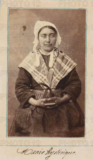 Portrait of a patient in a lunatic asylum, possibly Salpêtrière, photograph, : 'hysterical mania', c. 1860 - c. 1885, photographer, paper, albumen print, height 92 mm x width 56 mm, historical persons not known by name - BB - woman, lunatic asylum, mental home, emotional illness, derangement, madness, A sepia portrait of a seated woman wearing a light-colored cap with ties under her chin and a pleated ruffle at the side, a checked shawl draped over her shoulders, and a dark textured dress with a full skirt and gathered apron; her hands are clasped in her lap holding a small rectangular object, and she looks slightly toward the camera with a neutral expression, framed by a simple border on a light background.