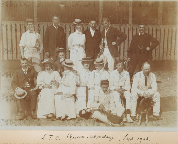 Group at tennis club LTC Quick-Advantage, Gerard Aalbersberg seated on the left, photograph, photographer: circle of Gerard Aalbersberg (us), The Hague, 1906-09, paper, daylight collodion silver print, height 130 mm x width 179 mm, A sepia photograph of a group of people posed outdoors in front of a wooden fence and wire mesh, arranged in three rows with some seated on the ground and others standing behind; men and women wear early twentieth-century clothing including light-colored dresses and blouses, suits, jackets, and straw boater hats, while one man holds a racket and another leans on a racquet, a seated man in the front holds a case, and a dog sits beside a man at the lower right.