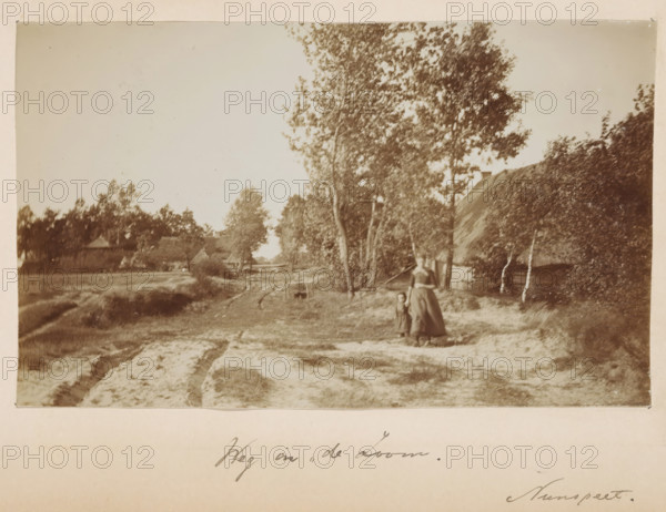 Farmer's wife and child on a small road in 'de Zoom' in Nunspeet, photograph, title: 'Road in 'de Zoom' Nunspeet', photographer: Gerard Aalbersberg (us), Nunspeet, c. 1897, Gerard Aalbersberg (us), photographer, paper, daylight collodion silver print, height 100 mm x width 164 mm, A sepia-toned outdoor scene showing a dirt path with ruts running into the distance, flanked by grassy and sandy ground; tall trees with leafy canopies line one side of the path and a thatched-roof building is partially visible behind foliage; a woman in a long dress stands near the trees holding the hand of a small child who wears a dark outfit; more trees and distant buildings are visible along the horizon under a pale sky.
