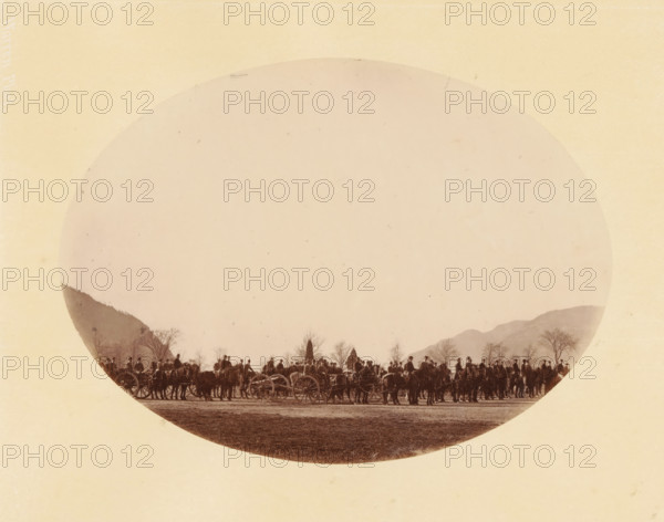 Cadets, West Point (original title), Group of Cadets of West Point, photograph, inscription: 'West Point, 1867, 225, ST1140', inscription: 'Warren Phot.', photographer: George Kendall Warren, North America, pasteboard, paper, albumen print, height 145 mm x width 198 mm, height 253 mm x width 330 mm, military instruction, American Civil War, A large circular sepia photograph centered on a pale rectangular background shows a long line of people and horses with carriages along a flat open area, with silhouettes of leafless trees and low mountains visible behind them; the scene is framed by the round edge of the photograph and the paper shows a textured, aged appearance.