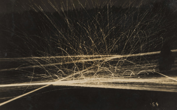 Barrage with machine gun(s) at evening or night, photograph, number: '54', name: 'PHOTO WIDMER, WALLENSTADT', inscription: 'Feu de barrage, 6 mitrailleuses, fM, ... illegible word', photographer: E. Widmer, c. 1930, paper, gelatin silver print, developing gelatin silver print, height 88 mm x width 139 mm, Dark background with many bright, thin streaks and arcs radiating upward and outward from a brighter horizontal band near the center, forming tangled, overlapping lines and curved trails that vary in length and curvature, with some straight horizontal lines crossing the scene and numerous short, arching marks concentrated near the lower center, all rendered in a pale, warm tone against the dark field.