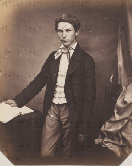Portrait of an unknown standing young man with hand on book, photograph, photographer: attributed to Franz Hanfstaengl, Germany, c. 1855 - c. 1860, Attributed to, paper, salted paper print, salt print, height 222 mm x width 154 mm, anonymous historical person depicted, A sepia-toned portrait of a young person standing and facing the camera, wearing a dark long coat over a light-colored waistcoat and a tied neck scarf; one hand rests on an open book placed on a draped surface while the other hand hangs by the side, and folded drapery is visible to the right.