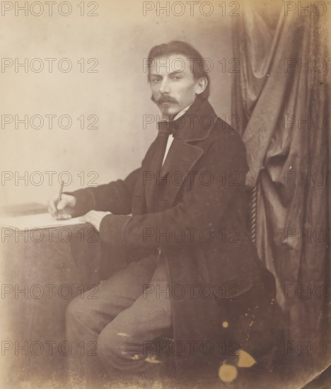 Portrait of Marggraf, architect, drawing with pencil in his hand, photograph, inscription: 'Marggraf Architekt', photographer: attributed to Franz Hanfstaengl, Germany, c. 1855 - c. 1860, Attributed to, paper, salted paper print, salt print, height 198 mm x width 163 mm, height 236 mm x width 294 mm, A seated man with a mustache and small goatee looks toward the camera while holding a pen over a sheet on a table, wearing a dark coat with wide lapels and a bow tie, with a curtain draped behind him and a plain light background on the other side, his visible arm resting on the table and his legs partially shown beneath the tablecloth.