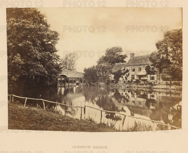 Godstow Bridge, View across the Thames, in the distance Godstow Bridge, photograph, page, photographer: attributed to Francis Frith, Godstow, c. 1862 - in or before 1867, Attributed to, paper, albumen print, height 100 mm x width 141 mm, river, Thames, A sepia-toned scene shows a river with a reflective surface bordered by grassy banks and a simple wooden fence in the foreground; a stone bridge with a wooden sluice structure spans the water toward the left, and on the right a stone house with a tiled roof sits amid trees and shrubs, its facade and windows visible; large trees frame both sides of the image and their reflections appear in the river, while the sky above is pale and largely uniform.