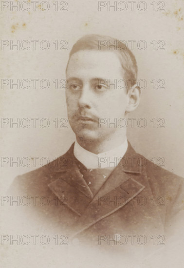 Portrait of a young man, album page, photograph, carte-de-visite, This photo is part of an album., inscription: 'ATELIER SPÉCIAL, DE REPRODUCTIONS, D'AGRANDISSEMENTS, ET PEINTURE A L'OUILE., L. van de Winkel, Photographie Parisienne, Rotterdam, 123. Rue Van Oldenbarnevelt 123.', photographer: Lodewijk van de Winkel, 1881 - 1900, paper, pasteboard, albumen print, height 83 mm x width 52 mm, historical persons, A sepia-toned portrait of a young man shown from the chest up wearing a dark suit jacket with visible lapels and a high white collar, his hair is neatly combed and he has a faint mustache, his expression is neutral and his gaze is slightly off to one side, the background is plain and light with subtle age spots and speckling across the photo.