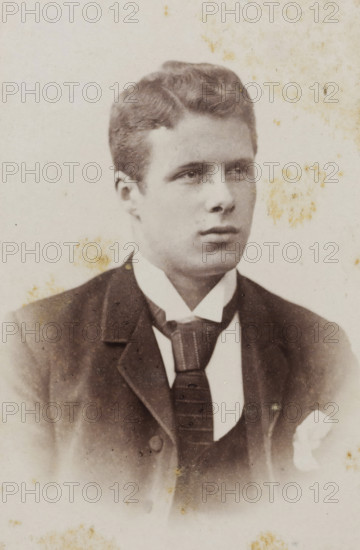 Portrait of a young man, album page, photograph, carte-de-visite, This photo is part of an album., inscription: 'H. Jonker, Apothekersdijk No. 7, Leiden., The printing plate is kept for further orders, Reproductions and Enlargements in all Genres', photographer: Hendrik Jonker, Leiden, 1872 - 1900, paper, pasteboard, albumen print, albumendruk, height 83 mm x width 52 mm, historical persons, A sepia-toned portrait of a young man shown from the chest up wearing a dark suit jacket and a high-collared shirt with a wide necktie; his hair is short and neatly combed with a slight wave, his face is clean-shaven with a neutral expression and his gaze directed slightly to the side, and the background is light with scattered faint stains and spots across the image.