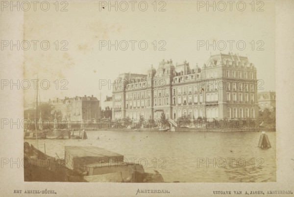 The Amstel Hotel. Amsterdam., View of the Amstel Hotel, photograph, cabinet photograph, Part of a Leporello album with 12 photographs of Amsterdam., photographer: attributed to Andries Jager, Amsterdam, c. 1860 - c. 1900, Attributed to, paper, pasteboard, albumen print, height 95 mm x width 135 mm, river, hotel, hostelry, inn, Amstel (river), Amstel Hotel, Professor Tulpplein, A waterfront scene shows a large multi-story building with ornate rooflines and many windows stretching along the shore, with steps and trees at its base; smaller buildings and architectural elements extend to the left; water occupies the foreground with a few boats and small sails visible near the shore; the image has a muted, aged tone and a pale border surrounding it.