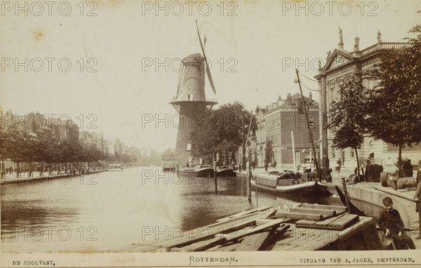 View of the Coolvest in Rotterdam with windmill De Hoop in the center, De Coolvest. Rotterdam., photograph, cabinet photograph, Part of a Leporello album with photos of Rotterdam., photographer: attributed to Andries Jager, Rotterdam, c. 1860 - c. 1900, Attributed to, paper, pasteboard, albumen print, height 95 mm x width 157 mm, windmill, Molen De Hoop, A riverside scene shows a large cylindrical windmill with long sails standing near the water, surrounded by trees and buildings with classical facades and ornate roof statues; boats are moored along the quay with cargo and barrels visible on deck, wooden planks and beams lie in the foreground near the water's edge, lampposts and telegraph poles line the street, and several people in period clothing stand or walk along the quay and near the buildings.