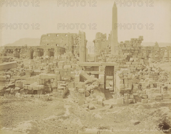South side of the Karnak temple complex, Karnak Ensemble du temple, côté sud, photograph, Part of Travel Album with 80 Photos of Egypt., negative number: '150', photographer: Maison Bonfils, Luxor, c. 1870 - c. 1898, North Africa, pasteboard, paper, albumen print, height 219 mm x width 282 mm, temple, shrine, Egyptian religion, A wide view of weathered stone ruins with scattered blocks and collapsed walls across a dusty foreground, rectangular stone lintels and doorways visible among stacked masonry, a tall obelisk rising centrally above the rubble, fractured columns and carved stone elements interspersed with rubble piles, a large partially intact wall in the background and low hills on the horizon, overall tones are pale and monochromatic.