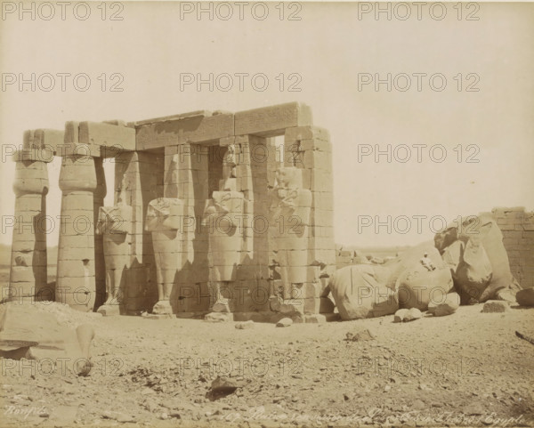 Overturned Statue of Sesostris in Thebes (Egypt), Overturned statue of Pharaoh Senusret (Sesostris) in Thebes (former title), Ramesseum (Temple of Ramses II), Thebes (Luxor), photograph, Part of Travel Album with 80 Photos of Egypt., negative number: '167', photographer: Maison Bonfils, c. 1870 - c. 1898, North Africa, Upper Egypt, pasteboard, paper, albumen print, height 221 mm x width 281 mm, monument, statue, Luxor, A row of tall stone columns and statues stands on a sandy, rocky ground, with several columns topped by square capitals and adjacent statues carved in a seated or standing pose, some of the statues appearing damaged or fragmented; a large broken statue with a visible head lies among scattered stone blocks and rubble to the right, while additional fallen fragments and stones are scattered across the foreground; a low stone wall or structure is visible behind the fallen pieces at the far right, and the sky above is clear and pale.