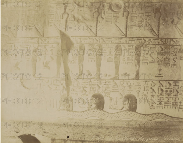 Tomb of Seti I (KV17) in the Valley of the Kings, Thebes (Luxor), Burial chamber of pharaoh Senuseret (Sesostris) in Thebes (former title), Thebes Tombe du grand Sesotris, photograph, Part of Travel album with 80 photos of Egypt., negative number: '943', photographer: Zangaki, C. & G., c. 1870 - c. 1890, North Africa, Upper Egypt, pasteboard, paper, albumen print, height 218 mm x width 276 mm, grave, tomb, Egyptian hieroglyphs, Luxor, A faded wall panel with carved figures and symbols in a monochrome sepia tone, showing vertical standing humanoid figures with headdresses aligned along horizontal bands, smaller bird and animal shapes interspersed among rectangular and linear carved motifs, repeating rows of hieroglyph-like pictorial signs, a large undulating serpent-like form along the lower band with patterned scales, partial human heads emerging above the serpent with visible facial features and hair, areas of surface wear and patched plaster with lighter and darker discolorations, an...