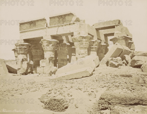 Koum-Ombos (Égypt), View of the Temple of Kom Ombo, photograph, Part of Travel album with 80 photos of Egypt., number: '89', negative number: '176', photographer: Maison Bonfils, Kom Ombo, c. 1870 - c. 1898, North Africa, pasteboard, paper, albumen print, height 220 mm x width 280 mm, temple, shrine, Egyptian religion, A sunlit ruin of a stone structure with rows of large carved columns topped by ornate capitals, some capitals shaped like stylized plant forms, stands amid scattered massive stone blocks and broken architectural fragments lying on a sandy, rubble-strewn ground, with horizontal lintels and a partially intact entablature showing carved reliefs above the columns and open spaces between the supports.