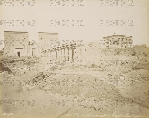 Phyloe. General view of the temples of Isis (Egypt), View of the Temples of Isis on the island of Philae, photograph, Part of a travel album with 80 photos of Egypt., negative number: '187', photographer: Maison Bonfils, Philae, c. 1870 - c. 1898, North Africa, pasteboard, paper, albumen print, height 222 mm x width 280 mm, The Temples of Isis on Philae were moved to the island of Agilkia between 1977 and 1980 due to the construction of the Aswan Dam., temple, shrine, Egyptian religion, Egypt, A wide, pale photograph of an ancient stone temple complex showing large, flat-topped walls and gateways with carved reliefs, a long colonnade of round columns with decorated capitals stretching diagonally across the middle ground, and a separate pavilion with clustered columns on the right, all set amid a foreground of uneven, rocky ground and scattered stone blocks.