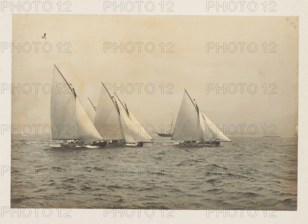 Various sailing ships, including the Windfall, launched, album page, photograph, This photo is part of an album., check stamp: 'Adamson, Rothesay.HB, Copyright', number: '3', photographer: attributed to James Adamson, c. 1880 - c. 1900, Attributed to, paper, gelatin silver print, developed gelatin silver print, height 190 mm x width 281 mm, sailing-ship, sailing-boat, landscapes with waters, waterscapes, seascapes (in the temperate zone), Several sailboats with tall triangular sails are shown on open water, their hulls cutting through small waves and producing spray, the sails mostly light in tone with visible seams and lines, a larger boat appears behind them, the sky above is pale and uniform, and the scene fills a framed photographic border.