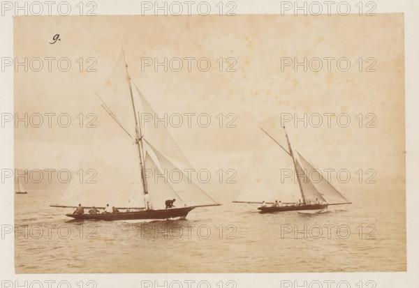 Sailing ships the Daisie and Olivette launched, album page, photograph, This photo is part of an album., check stamp: 'Adamson, Rothesay.HB, Copyright', number: '9', photographer: attributed to James Adamson, c. 1880 - c. 1900, Attributed to, paper, albumen print, height 190 mm x width 288 mm, sailing-ship, sailing-boat, landscapes with waters, waterscapes, seascapes (in the temperate zone), A sepia-toned photograph showing two sailboats on calm water, each with tall masts and triangular sails partially unfurled, with crew members positioned along the hulls and one person crouched near the bow of the left boat, distant shoreline visible on the left, and a small solitary boat near the horizon.