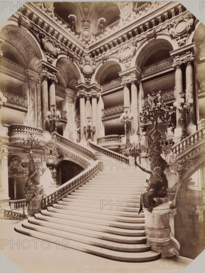 Interior with stairs of the Opéra de Paris, album page, photograph, This photo is part of an album., inscription: '478 - Paris. l'escalier du Grand-Opéra. Ed. H. édit', photographer: Edouard Hautecoer (possibly), Paris, publisher: Edouard Hautecoer, 1890 - 1898, Edouard Hautecoer, photographer, publisher, paper, albumen print, albumendruk, height 258 mm x width 355 mm, staircase, opera house, Opéra de Paris, A wide marble staircase with sweeping curved steps ascends between ornate balustrades, flanked by sculpted figures mounted on pedestals holding candelabras; tall Corinthian columns rise behind the balustrades supporting a richly decorated entablature with carved medallions and reliefs, and a series of large rounded arches reveal upper-level balconies with intricate wrought-iron railings; elaborate chandeliers and multiple lamp fixtures with globes hang and stand throughout the space, while carved ornamental details, garlands, and festoons decorate the arches and vaults above.
