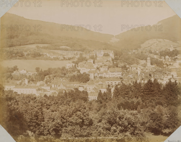 View of Baden-Baden, album page, photograph, This photo is part of an album., annotation: 'Reis Herrenalb. Baden-Baden, Wiesbaden. August 1899', inscription: '1666 Baden-Baden Panorama vom Friesenberg', photographer: LL, Baden-Baden, 1890 - 1899, Baden-Württemberg, paper, albumen print, albumendruk, height 258 mm x width 355 mm, city-view in general, 'veduta', A wide sepia-toned panorama shows a town nestled in a valley with rooftops and clustered buildings rising from a wooded foreground toward a lakeshore and surrounding hills, with a church tower and various multi-story structures among trees, terraced fields and patches of open land on the slopes, dense forest in the foreground and tree-covered hills framing the scene under a pale sky.