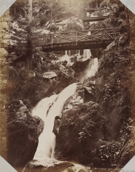 View of the Gertelbach Waterfalls, album page, photograph, This photo is part of an album., inscription: '894 Gertelbach - Baden. Waterfalls. LL', photographer: LL, Baden-Baden, 1890 - 1899, Baden-Württemberg, paper, albumen print, height 258 mm x width 355 mm, waterfall, A sepia-toned photograph showing a rocky forested ravine with cascading water flowing downward over smooth rock surfaces and between boulders, a wooden footbridge with a simple log railing crossing the stream partway up, trees and dense vegetation clinging to the steep rock faces on either side, smaller wooden railings and walkways visible higher up along the slope, wet moss and ferns on the rocks, and streaks of flowing water captured with a silky appearance.