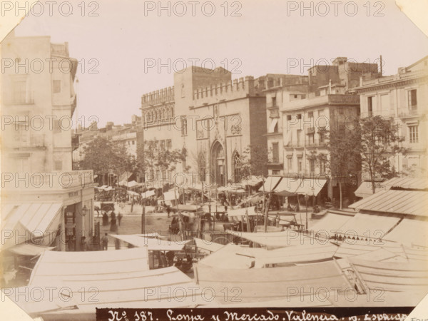 Market in Valencia, Lonja y Mercado. Valencia, album page, photograph, This photo is part of an album., number: '187', annotation: 'Valencia - Marketplace and Bullring', photographer: Antoni Esplugas, Valencia, c. 1888 - in or before 1892-04-07, paper, albumen print, height 161 mm x width 214 mm, market, A wide street scene showing rows of market stalls with canvas canopies extending across the foreground and middle ground, a crowd of people moving between the stalls, a few horse-drawn vehicles among them, and taller buildings lining the background including a large ornate façade with arched doorways and decorative stonework flanked by multi-story residential and commercial buildings with balconies and windows, as well as several trees rising between the buildings.