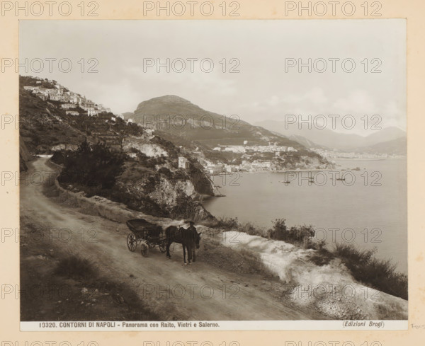 View of Raito, Vietri sul Mare and Salerno, Contorni di Napoli - Panorama con Raito, Vietri e Salerno, photograph, Part of Photo album with recordings of sights and works of art in Italy., number: '10320', photographer: Edizioni Brogi, Salerno (province), c. 1875 - in or before 1907, paper, gelatin silver print, developing gelatin silver print, height 200 mm x width 250 mm, city-view in general, 'veduta', rocky coast, Campagna, Vietri sul Mare, Raito, A coastal scene shows a dirt road running along a hillside with a horse-drawn carriage and driver on the roadside, the horse facing the viewer and the carriage behind it; the road curves toward a village built on terraced slopes with clustered buildings climbing the hillside, and cliffs dropping to a calm bay where several sailing vessels float on the water; distant mountains rise behind the coastal town under a cloudy sky, and vegetation and rocky outcrops line the road and slopes.